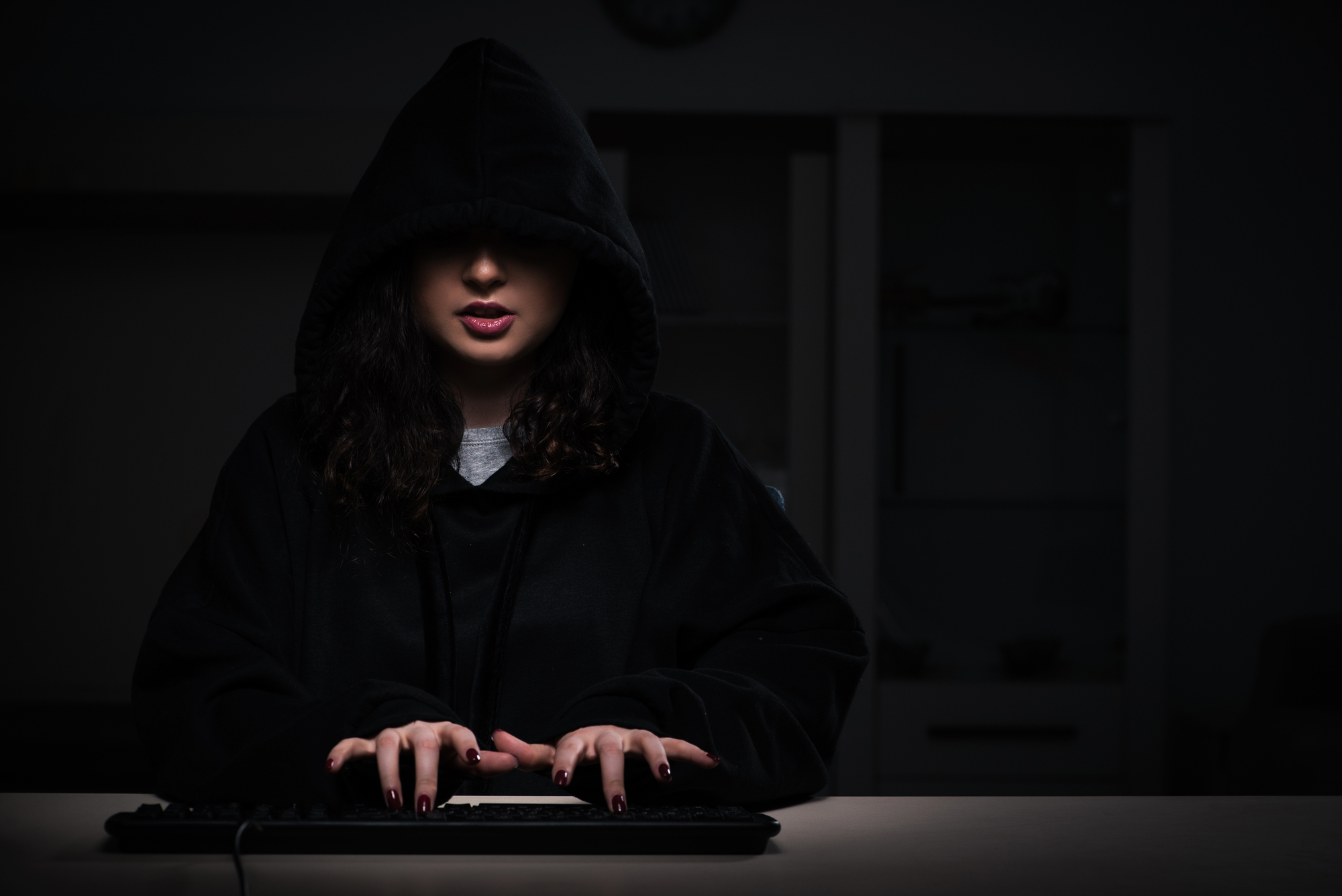 A woman in a black hoodie typing on a computer.