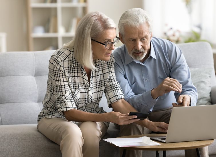 An older couple with bad credit looking at a laptop while sitting on a couch.