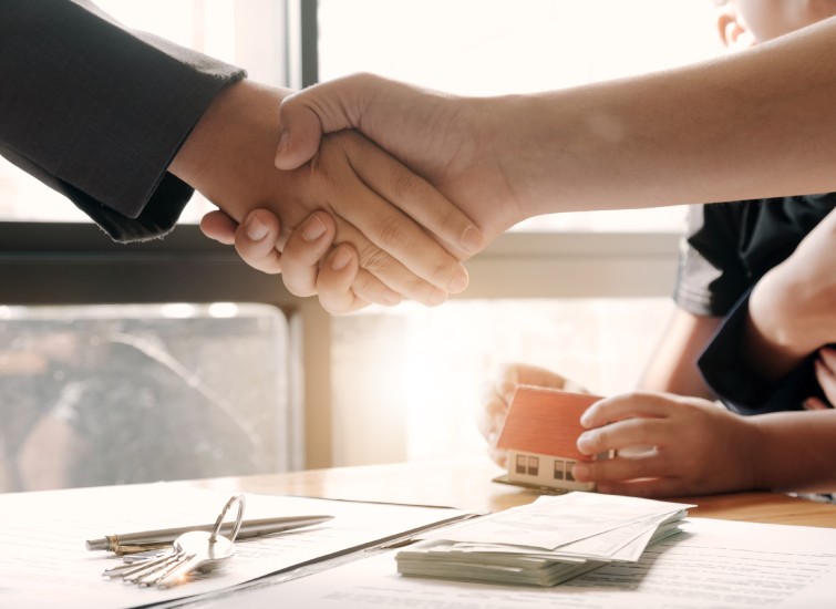 Two real estate professionals shaking hands in front of a table.