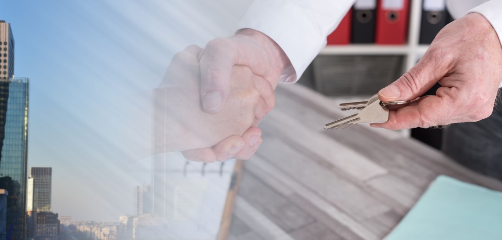 A man is shaking hands with a key in front of a real estate building.