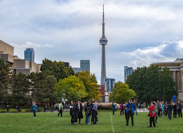 A group of people standing on a grassy field with the CN Tower, one of the iconic green buildings, in the background.