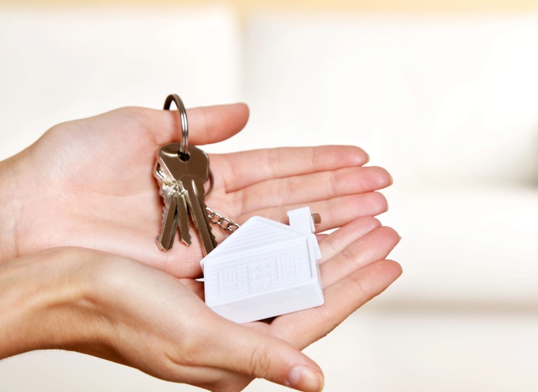 Hands holding a set of keys with a plastic keychain shaped like a house, symbolizing the excitement of new housing construction.