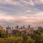 Panoramic view of the Metro Detroit skyline at dusk with scattered clouds and scattered buildings surrounded by trees.
