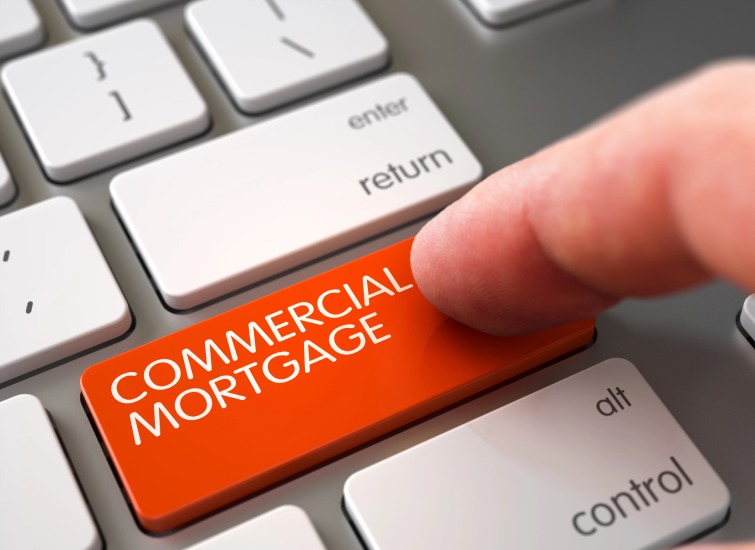 A finger presses a red keyboard key labeled "COMMERCIAL MORTGAGE" situated between the keys "enter" and "alt.