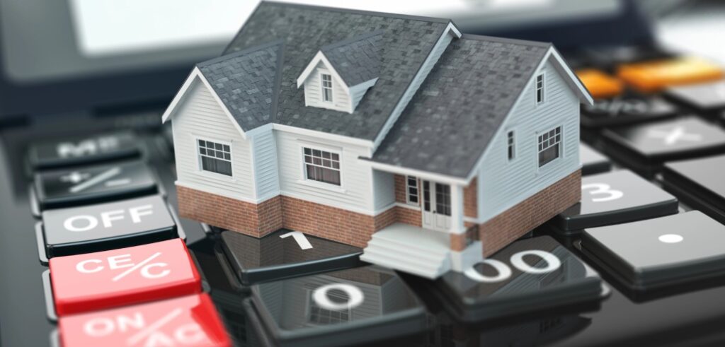 A model house sits on a calculator, symbolizing the financial considerations involved in purchasing a home.