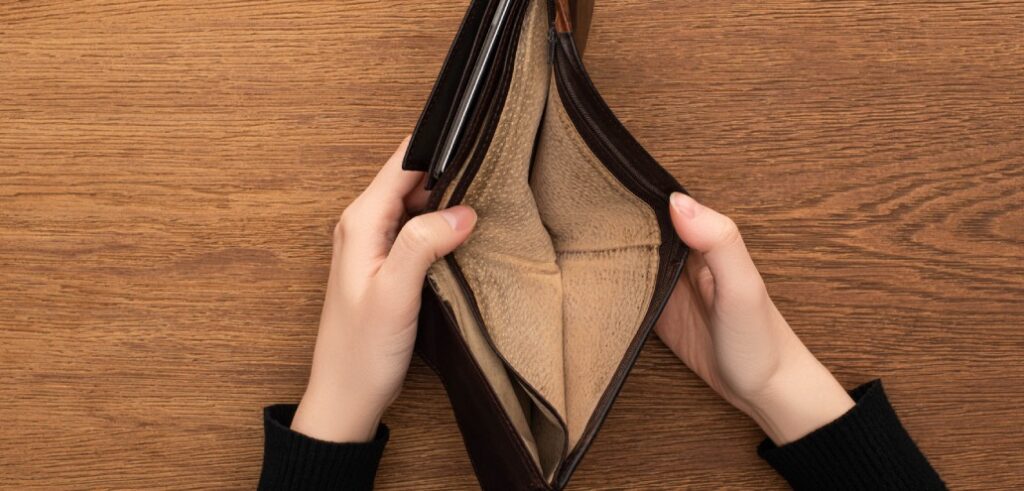 Hands holding an open, empty brown wallet over a wooden surface, symbolizing the financial weight of a looming mortgage.