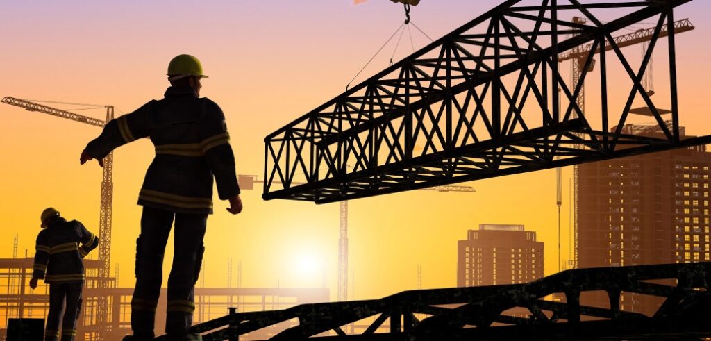 Construction workers wearing safety gear guide a metal beam being lifted by a crane at a construction site during sunset. Numerous cranes and unfinished buildings are visible in the background.