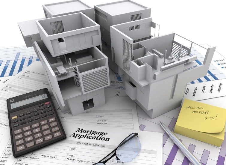 Scale model buildings on top of mortgage application papers, calculator, charts, pen, glasses, and sticky note.